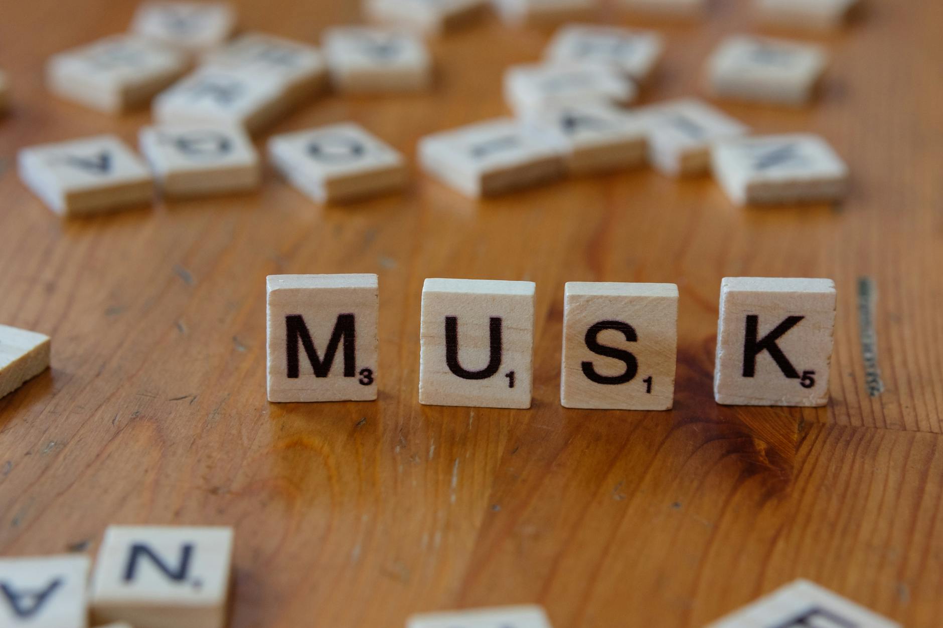 scrabble tiles spelling musk on wooden surface